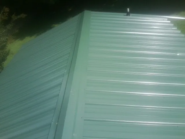 New green metal panels meeting at the ridge of a roof — Flat Roof Repair work by our crew in Boyce