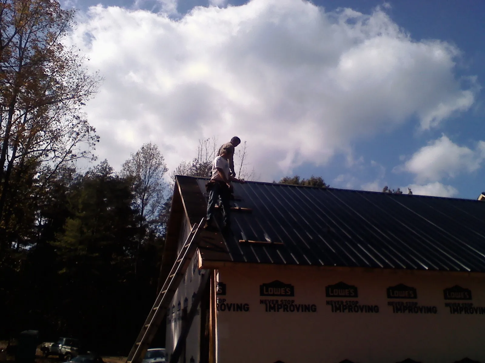 Roofer fastening dark metal panels high against a cloudy sky, from a Roof Inspection job in Boyce