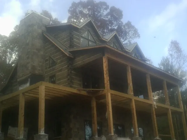 Stone chimney and dormers on a large log home with a timber porch in Boyce