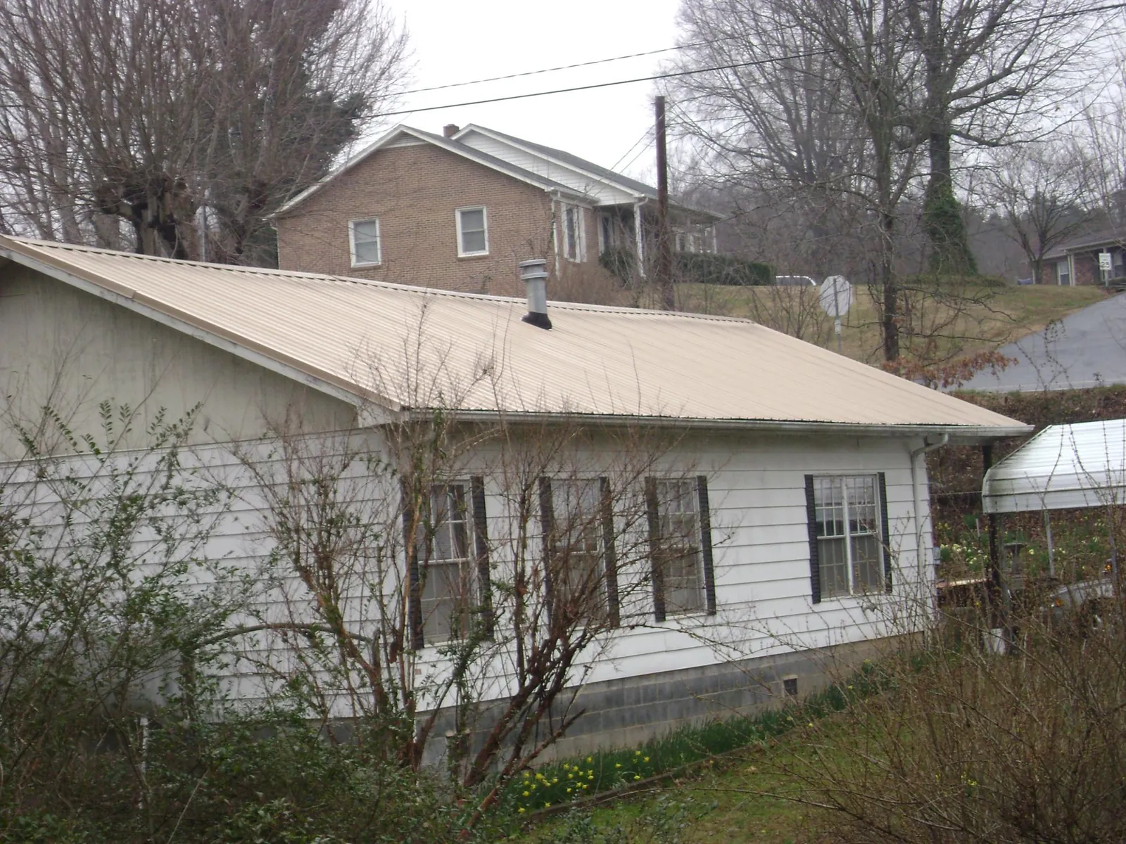 Tan metal roof on a white sided house set into a hillside — Commercial Roofing by Roofing Brothers in Boyce