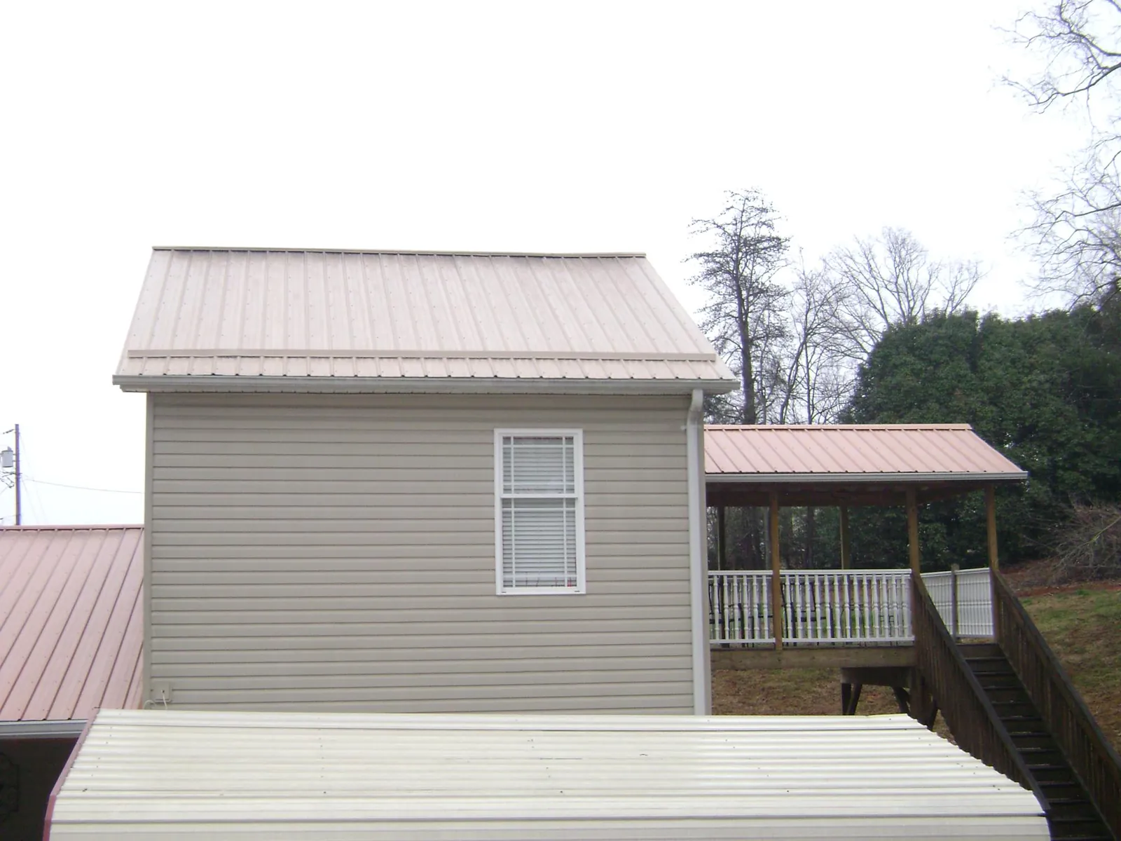 Tan metal roofs on a two story addition and attached porch, from a Roof Replacement job in Boyce